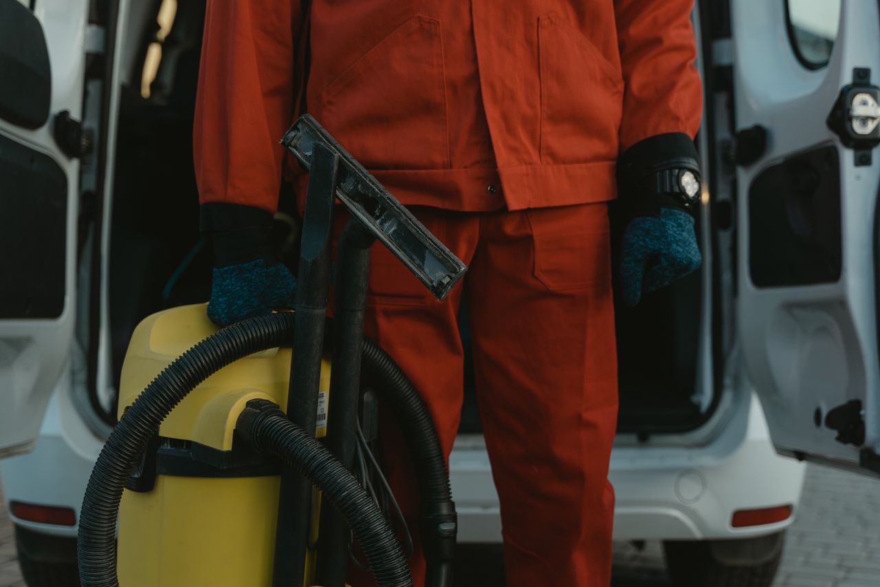 about-02 A professional cleaner in a red uniform holding a vacuum near a van, ready for service.